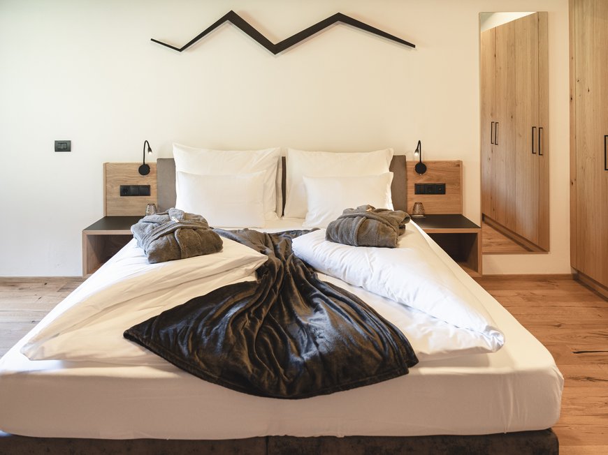 Aktivurlaub am Rosskopf bei Sterzing: Hotel Lahnerhof Modernes Schlafzimmer mit Doppelbett, Bademänteln und Holzschränken