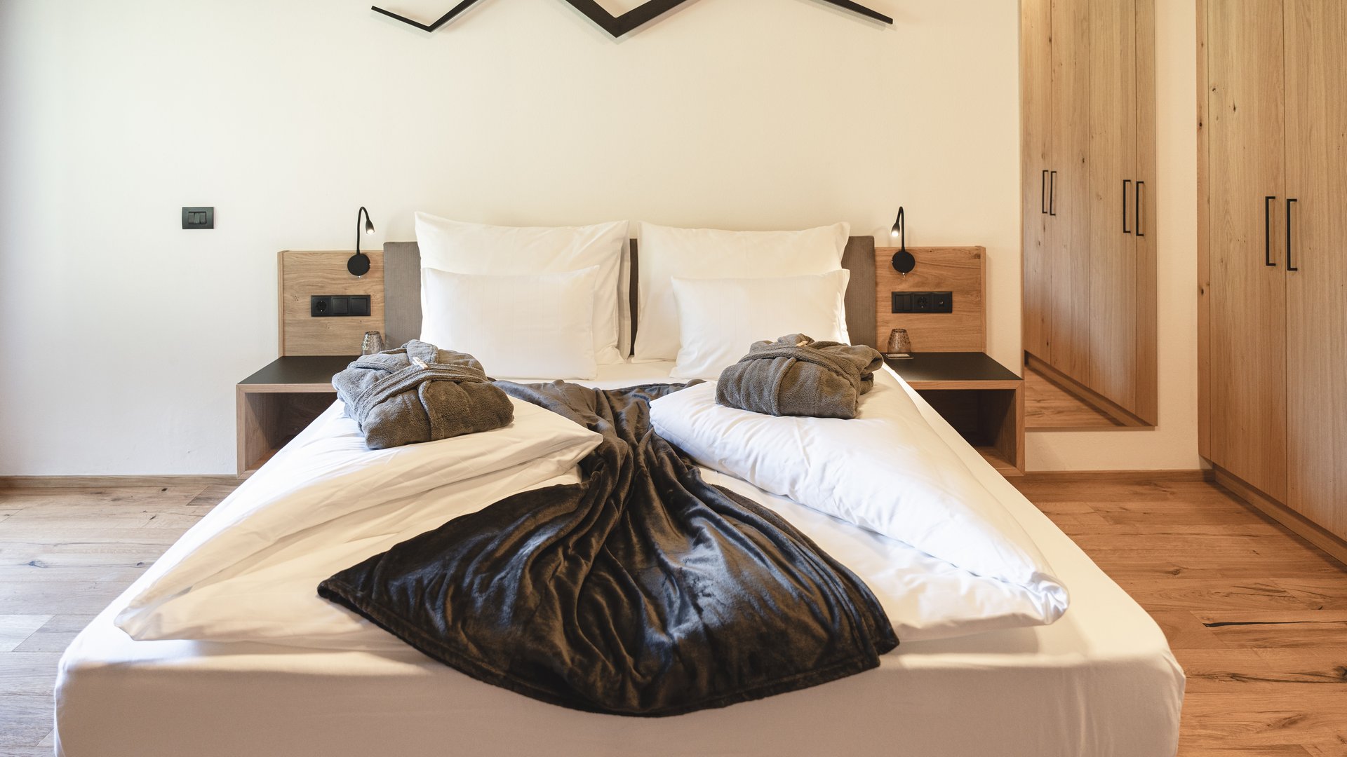 Aktivurlaub am Rosskopf bei Sterzing: Hotel Lahnerhof Modernes Schlafzimmer mit Doppelbett, Bademänteln und Holzschränken