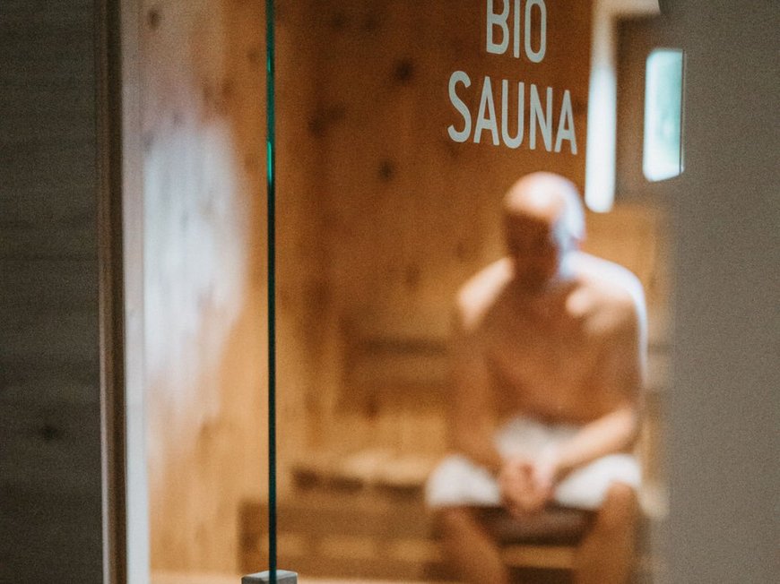 Wander- und Wellnesshotel bei Sterzing: der Lahnerhof Verliebter Mann sitzt in einer Bio-Sauna hinter Glastür