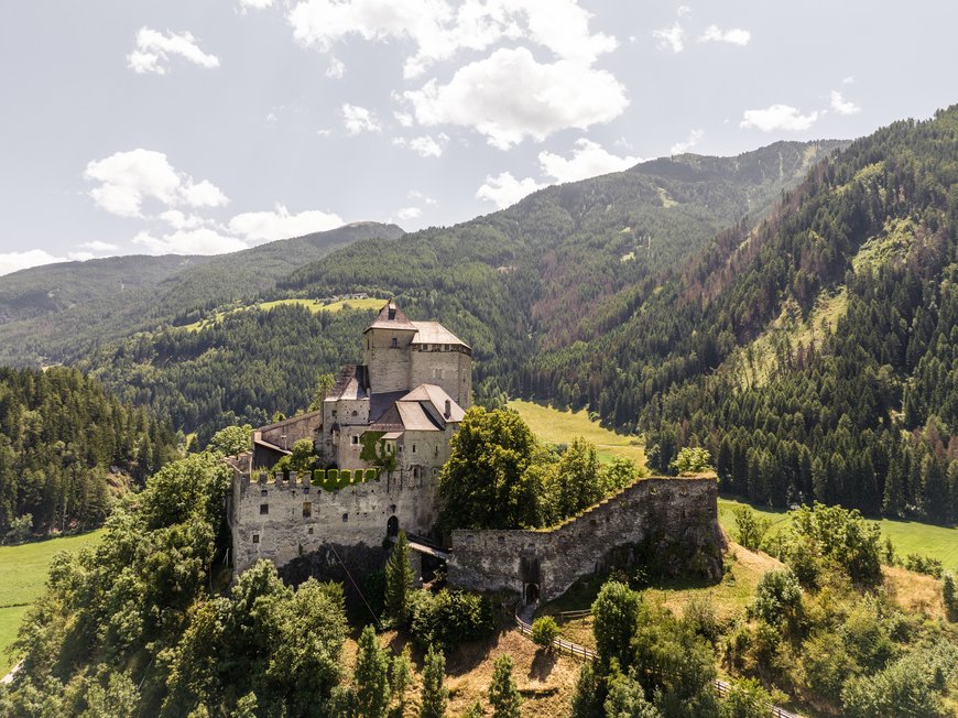 Hiking in Ratschings and surroundings Old castle with forested mountains and blue sky
