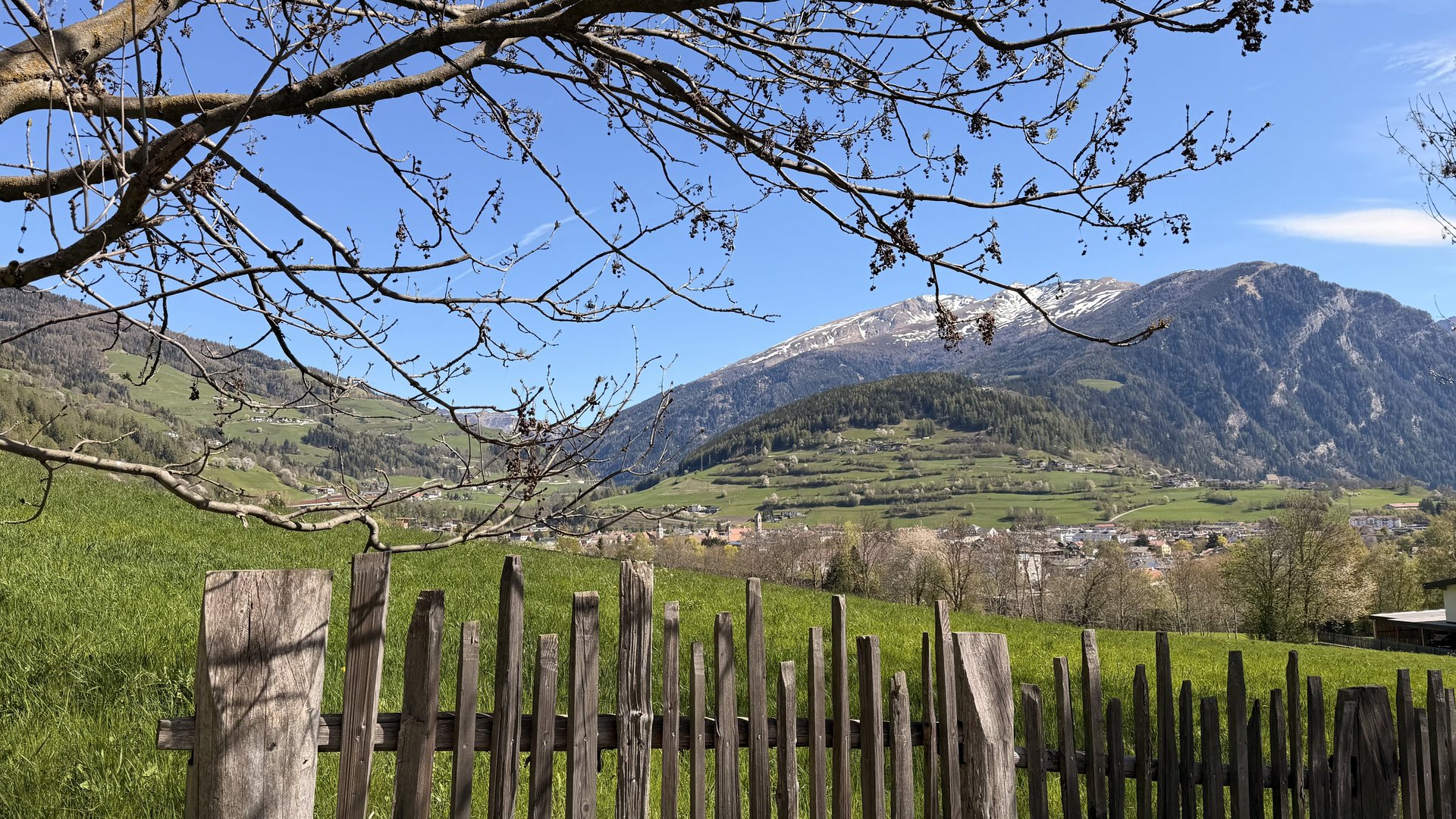 Entspannend und erlebnisreich Trockene Baumäste über Holzzaun mit Bergen und Dorf im Hintergrund