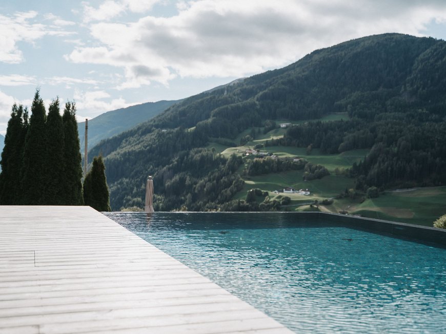 Lahnerhof, Ihr Hotel bei Sterzing Seeblick mit Pool und Bergen im Hintergrund bei bewölktem Himmel