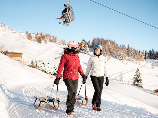 Lahnerhof: our hotel near Sterzing on Monte Cavallo/Rosskopf Two women with sleds on snowy slope under chairlift
