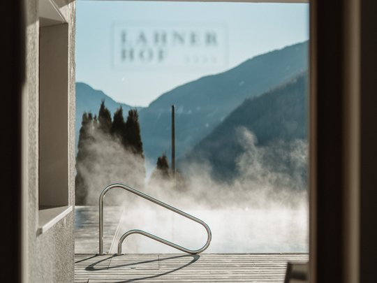 Cercate un hotel a Vipiteno con spa? Benvenuti al Lahnerhof! Vasca termale esterna con vista sulle montagne e pavimento in legno