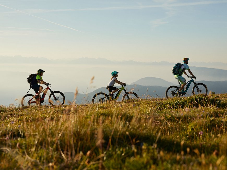 Delizioso ed entusiasmante Tre ciclisti con caschi pedalano su una collina erbosa in una giornata limpida