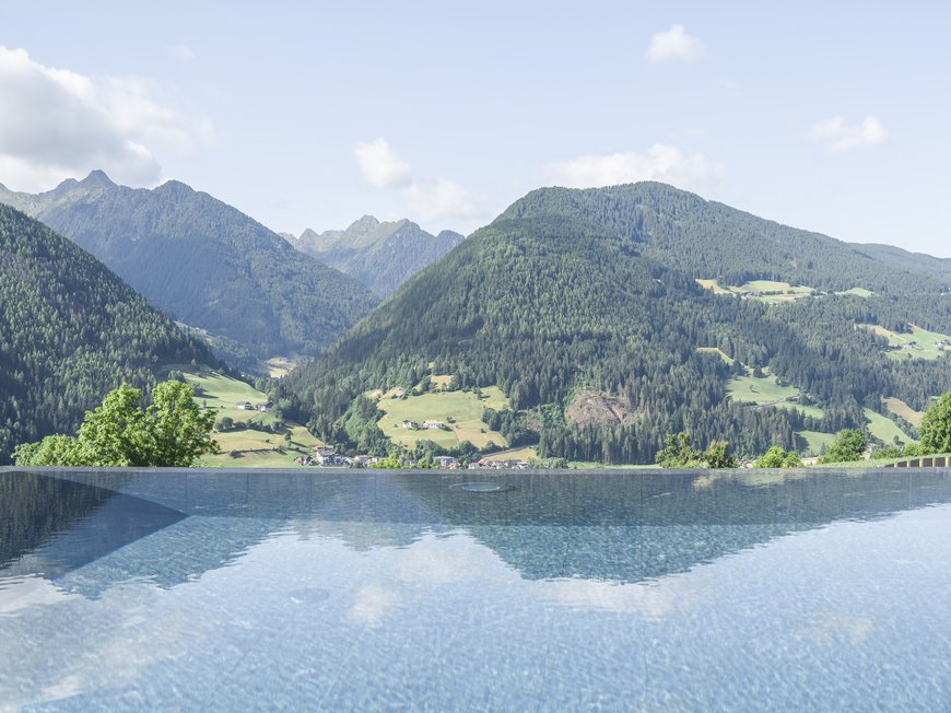 Lahnerhof, Ihr Hotel bei Sterzing Infinity-Pool mit Blick auf grüne Berge und bewölkten Himmel