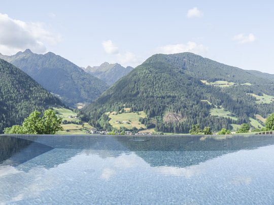 Our hiking and wellness hotel near Sterzing: Lahnerhof Infinity pool overlooking green mountains and cloudy sky