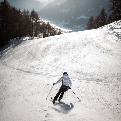 Hotel near Sterzing for wellness and sports Skier in white jacket skiing on snowy slope with mountains in the background