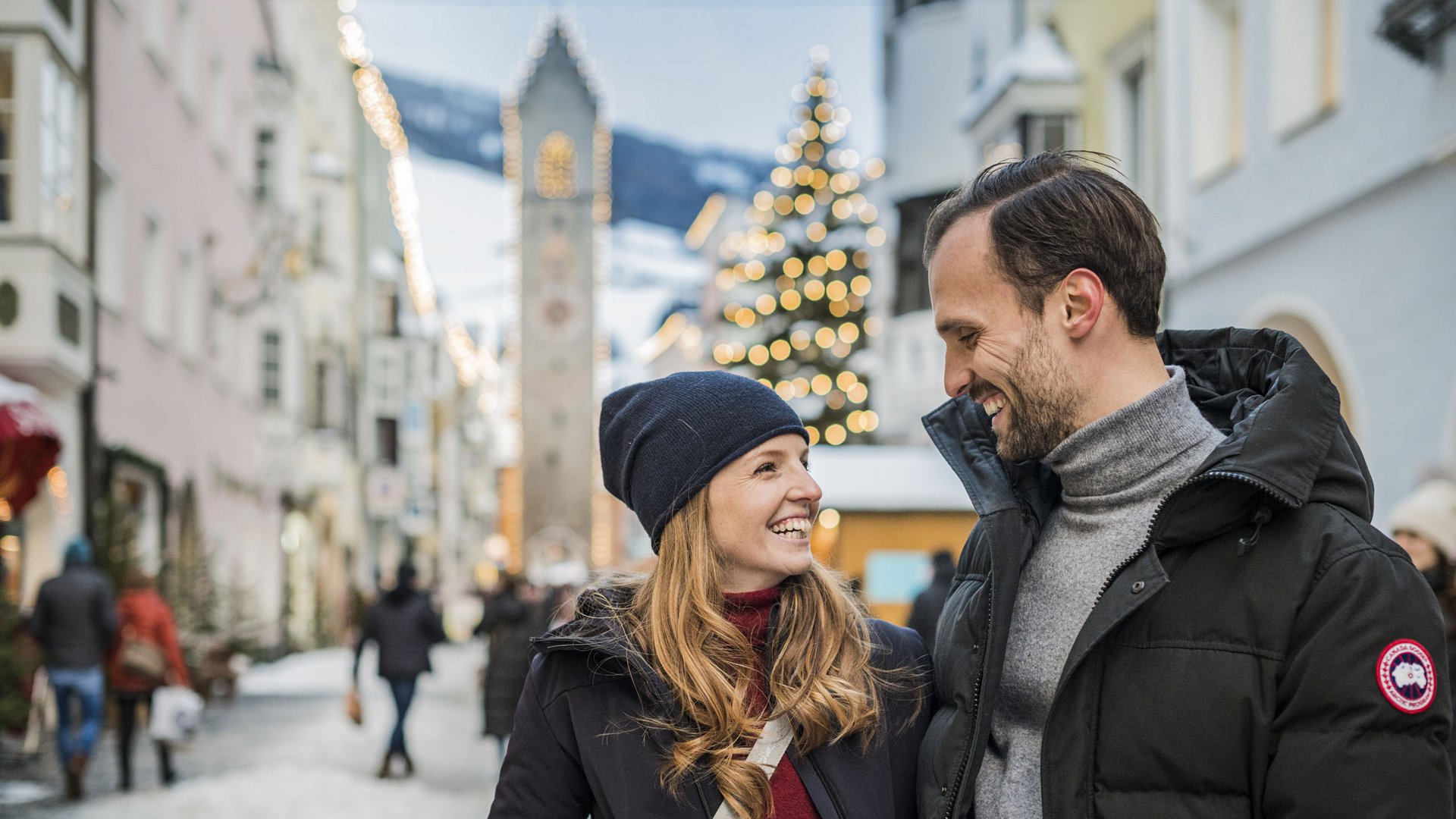 Wanderung auf den Rosskopf und mehr Paar lacht in winterlicher Altstadt mit Weihnachtsbaum und Turm im Hintergrund