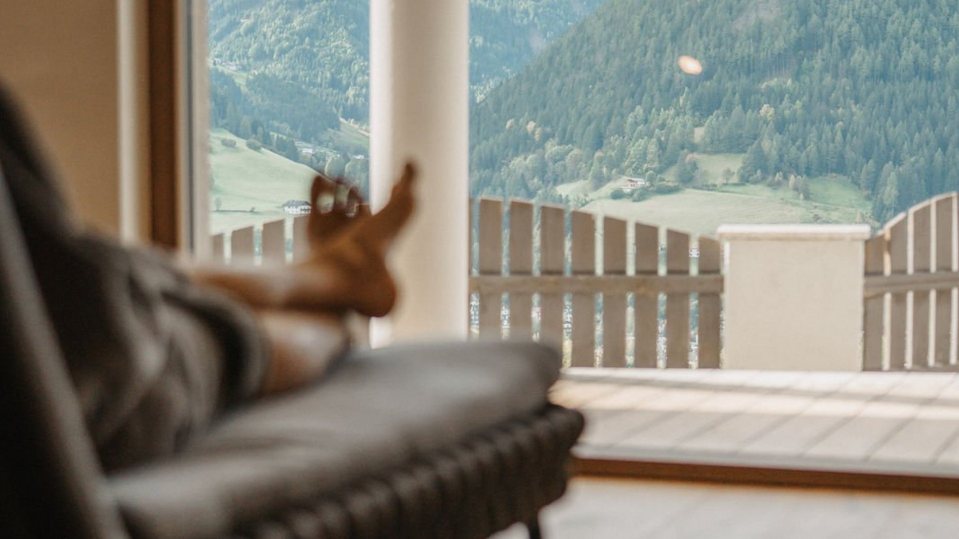 Lahnerhof, Ihr Hotel bei Sterzing Blick von innen auf Berge durch großes Fenster mit entspannter Person auf Sessel