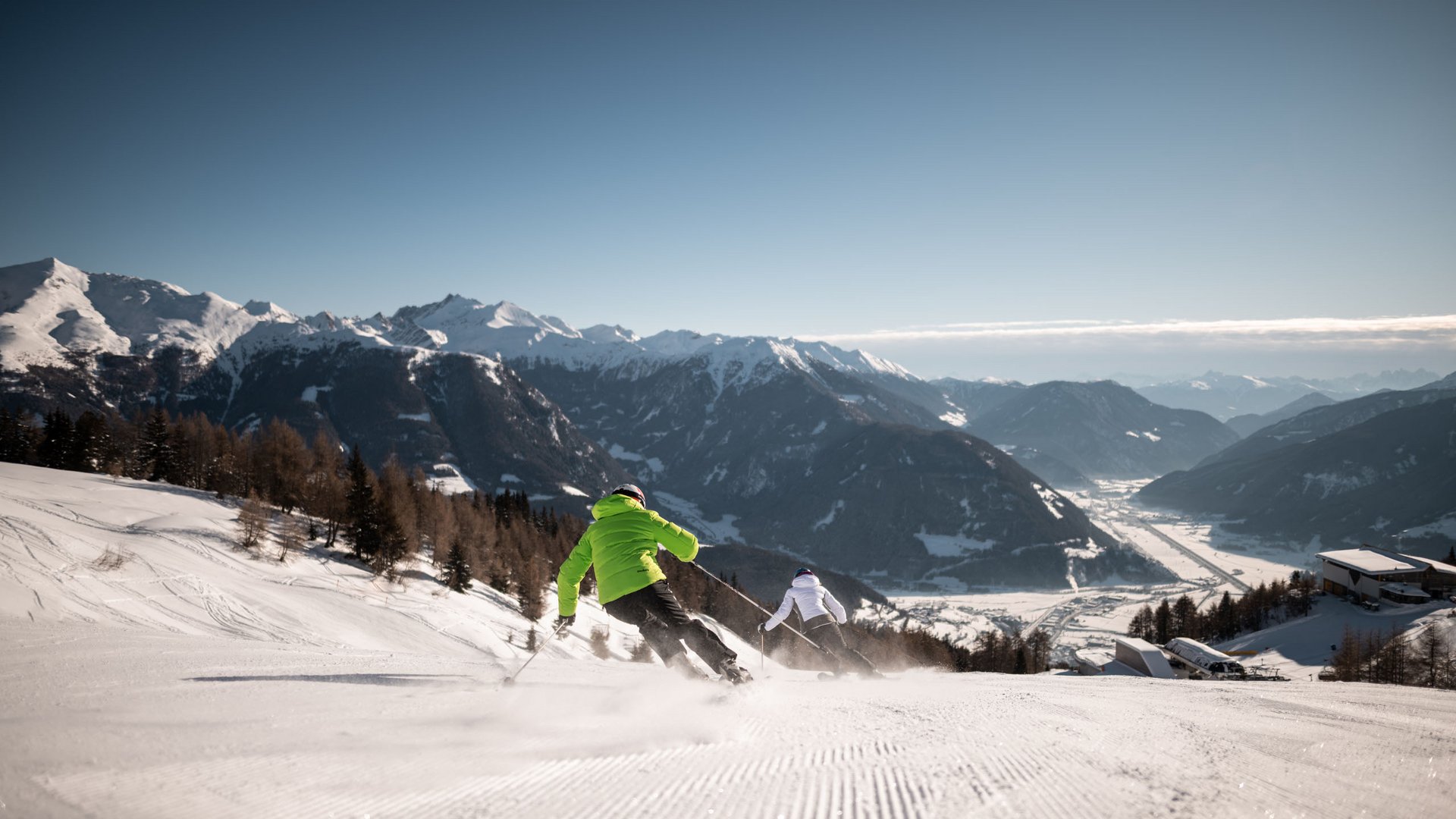 Lahnerhof: Natur- und Wellnesshotel bei Sterzing Zwei Skifahrer fahren einen schneebedeckten Hang mit Bergen im Hintergrund hinunter