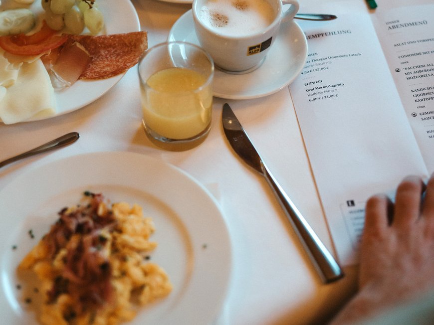 South Tyrolean specialities at our restaurant near Sterzing Breakfast with coffee, croissant, cheese, grapes, and scrambled eggs on white tablecloth