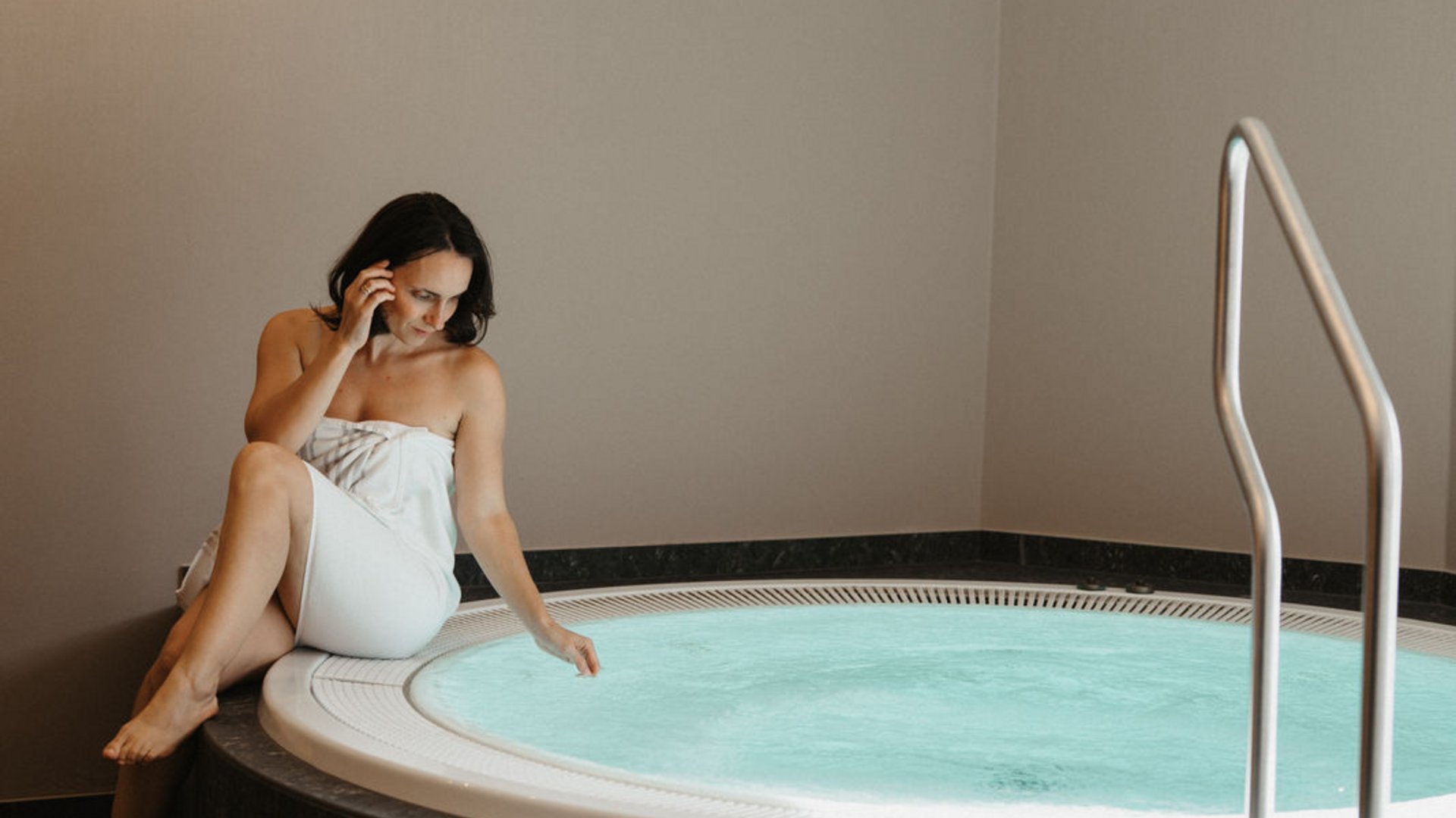 Cercate un hotel a Vipiteno con spa? Benvenuti al Lahnerhof! Donna con asciugamano bianco seduta sul bordo di una vasca idromassaggio riscaldata
