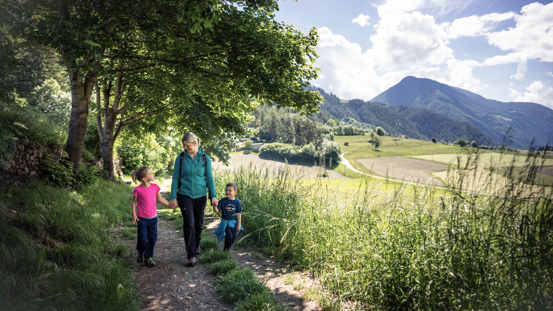 Entspannend und erlebnisreich Frau geht mit zwei Kindern auf einem Waldweg in den Bergen spazieren