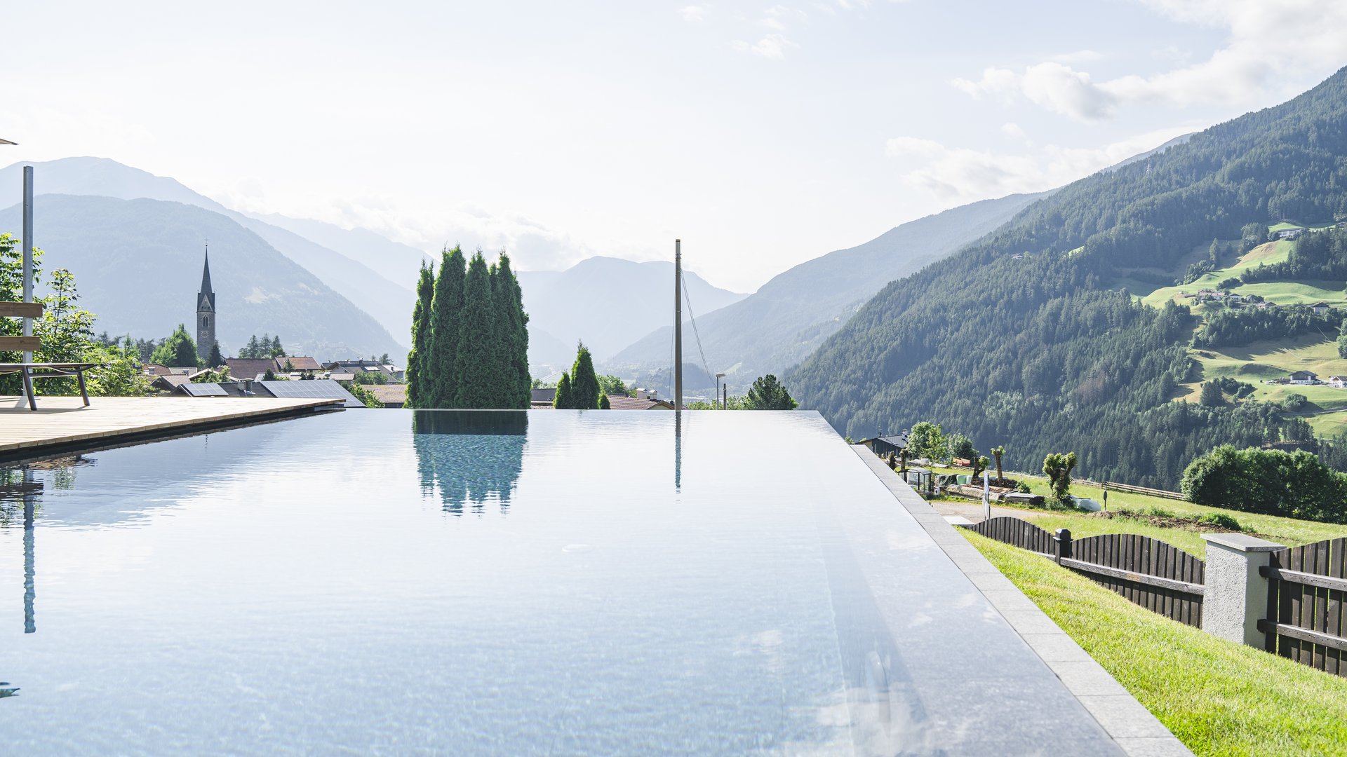 Our hiking and wellness hotel near Sterzing: Lahnerhof Infinity pool overlooking mountain village and green valleys on a sunny day