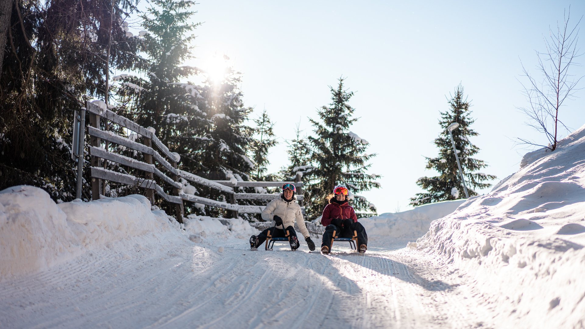 Wanderung auf den Rosskopf und mehr Zwei Personen rodeln den verschneiten Weg bei Sonnenschein hinunter