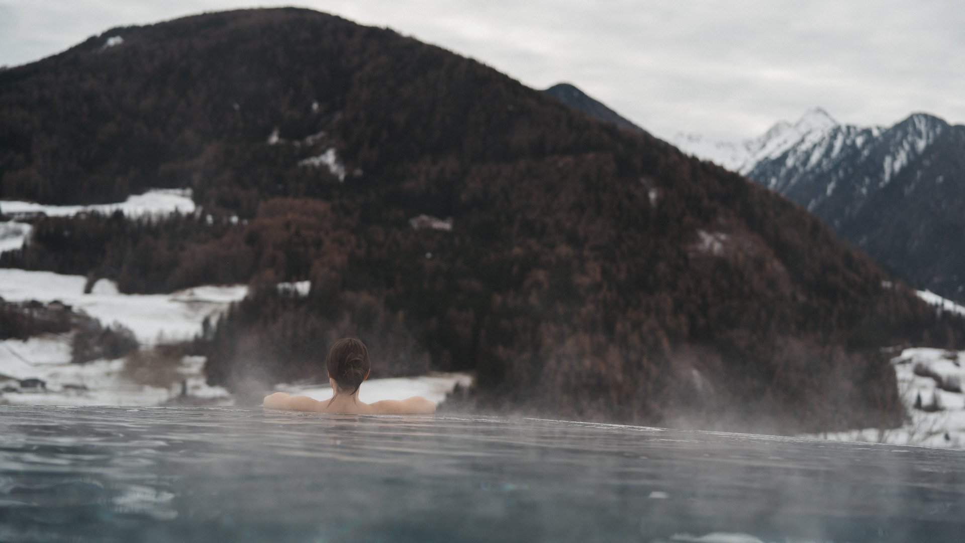 Lahnerhof: Natur- und Wellnesshotel bei Sterzing Person entspannt in einem dampfenden Außenpool mit verschneiten Bergen im Hintergrund