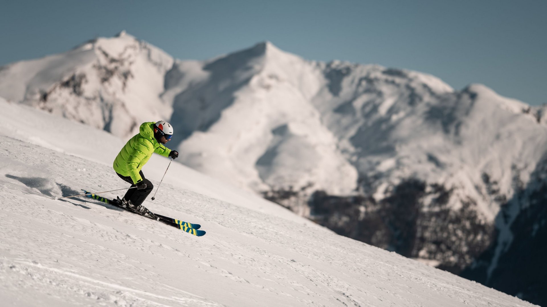 Wanderung auf den Rosskopf und mehr Skifahrer in grüner Jacke fährt auf verschneitem Berg mit schneebedeckten Gipfeln im Hintergrund
