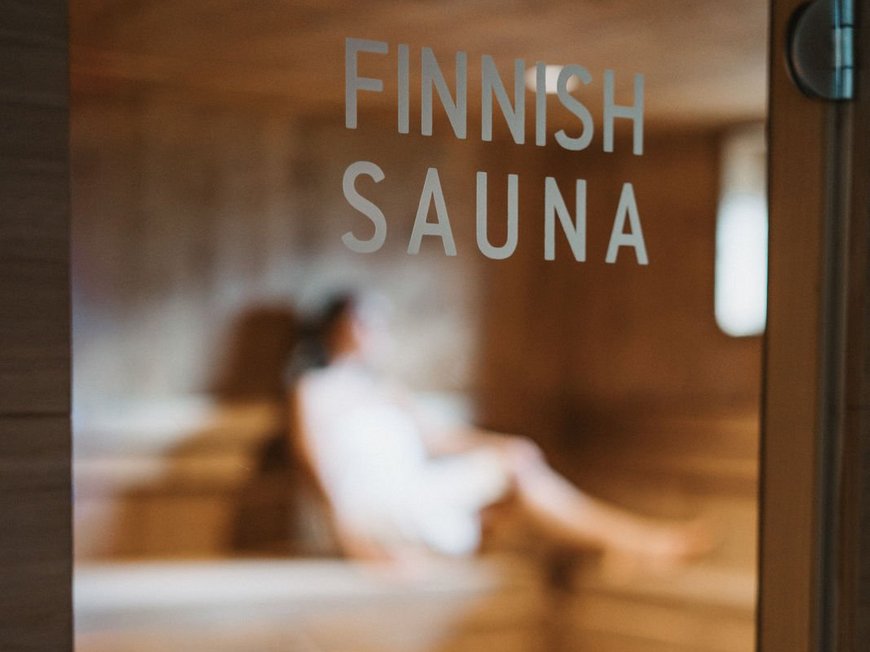 Cercate un hotel a Vipiteno con spa? Benvenuti al Lahnerhof! Porta con scritta sauna finlandese e persona sfocata all'interno