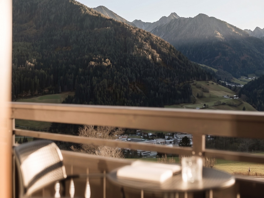 Vacanze al Monte Cavallo: eccovi all’Hotel Lahnerhof! Paesaggio montano con foresta e vallata visto da un balcone con sedia e tavolo