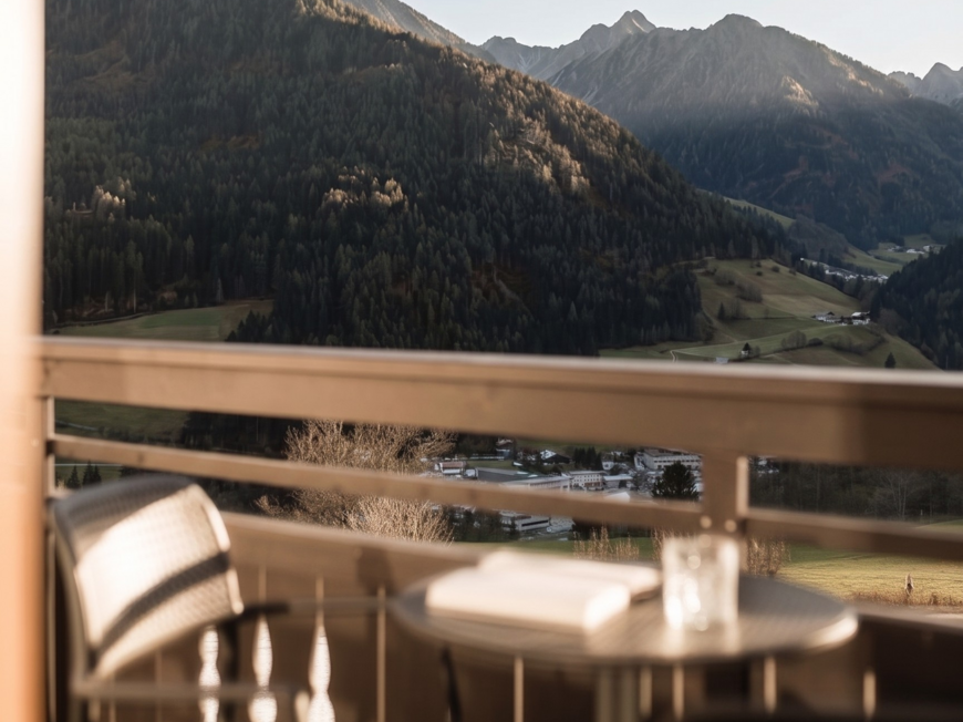 Aktivurlaub am Rosskopf bei Sterzing: Hotel Lahnerhof Berglandschaft mit Wald und Tal von einem Balkon mit Stuhl und Tisch aus gesehen