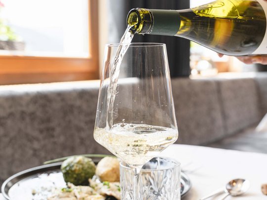 Benvenuti nel ristorante del nostro hotel con spa a Vipiteno Vino bianco versato in un bicchiere su un tavolo apparecchiato