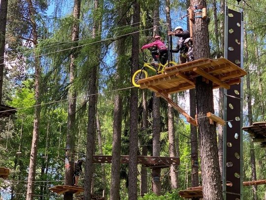 Hiking in Ratschings and surroundings Child rides bike on platform in high ropes course wearing safety harness