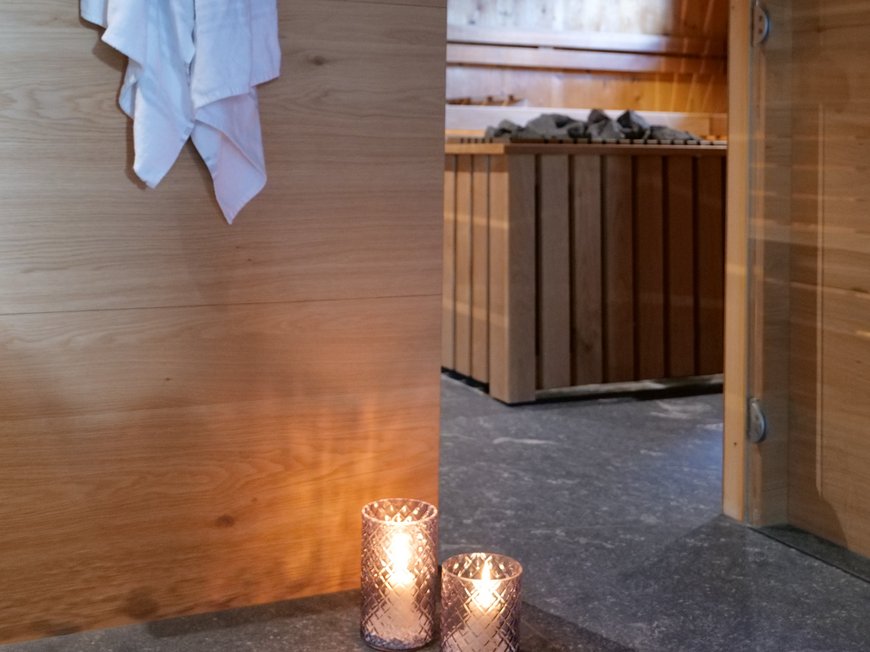 Lahnerhof, Ihr Hotel bei Sterzing Weiße Handtücher hängen neben einer Sauna mit brennenden Kerzen davor