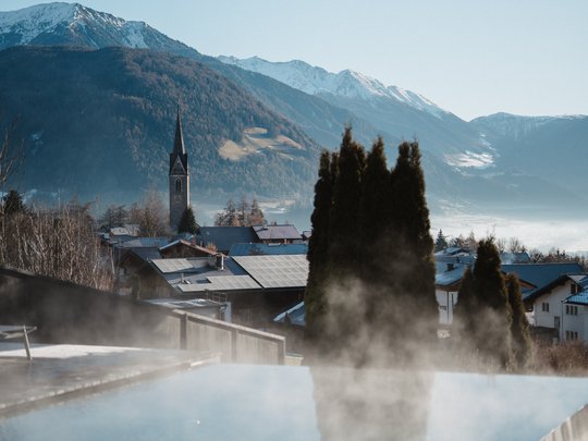 Cercate un hotel a Vipiteno con spa? Benvenuti al Lahnerhof! Vista di un villaggio di montagna con chiesa e montagne innevate sullo sfondo