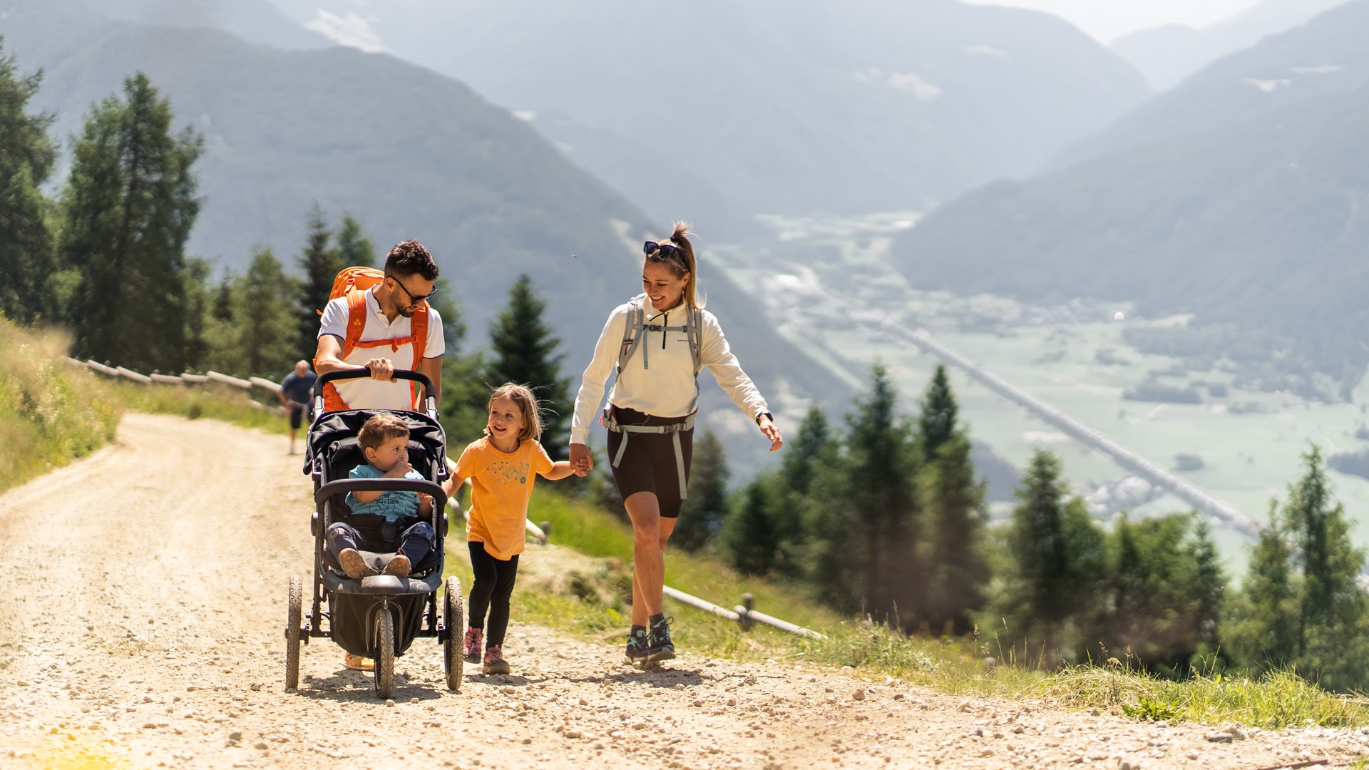 Köstlich und erlebnisreich Familie wandert mit Kinderwagen auf bergigem Wanderweg bei Sonnenschein