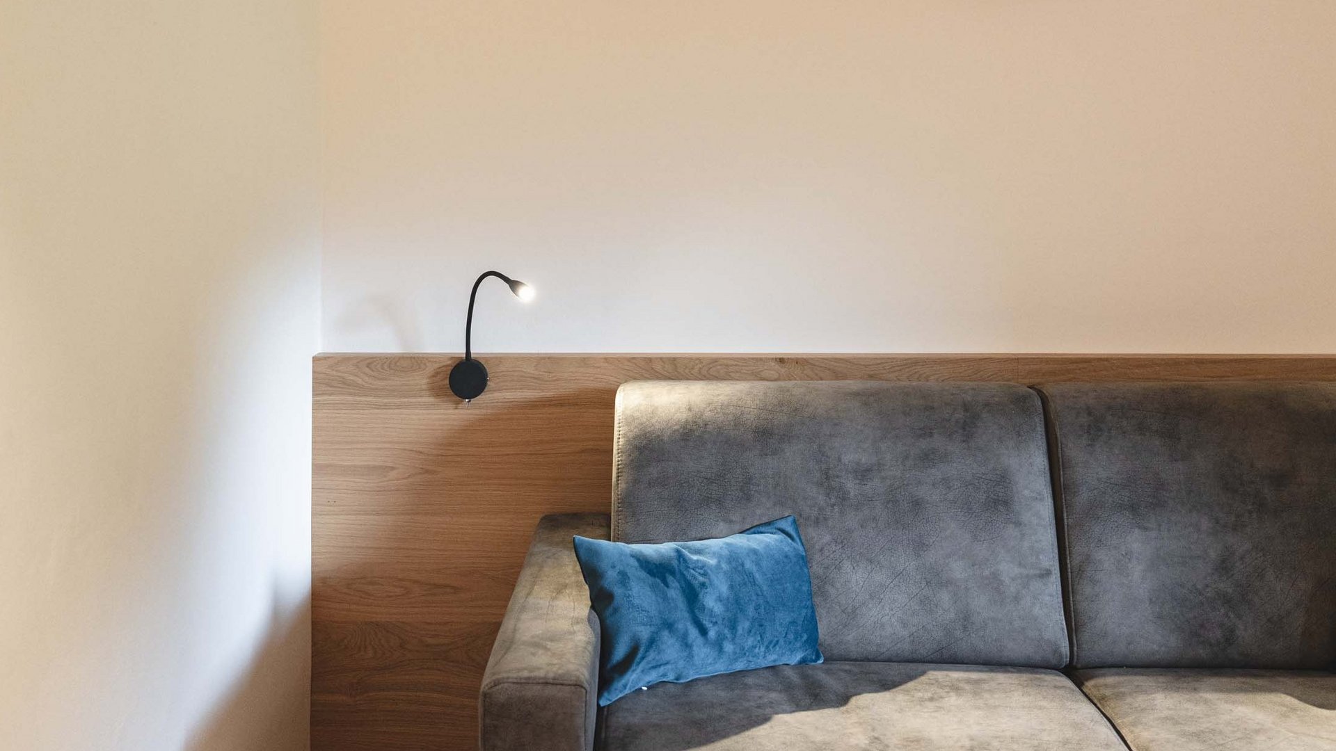 Lahnerhof, Ihr Hotel bei Sterzing Grau bezogenes Sofa mit blauen Kissen und modernem Leseleuchte an Holzwand