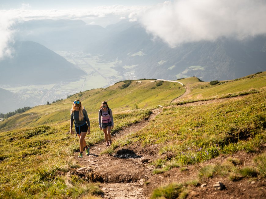 Hiking in Ratschings and surroundings Two women hiking on a mountain trail with valley view and clouds in the background