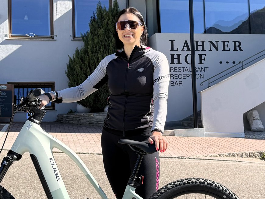 Our hiking and wellness hotel near Sterzing: Lahnerhof Woman with bicycle in front of Lahner Hof hotel on a sunny day
