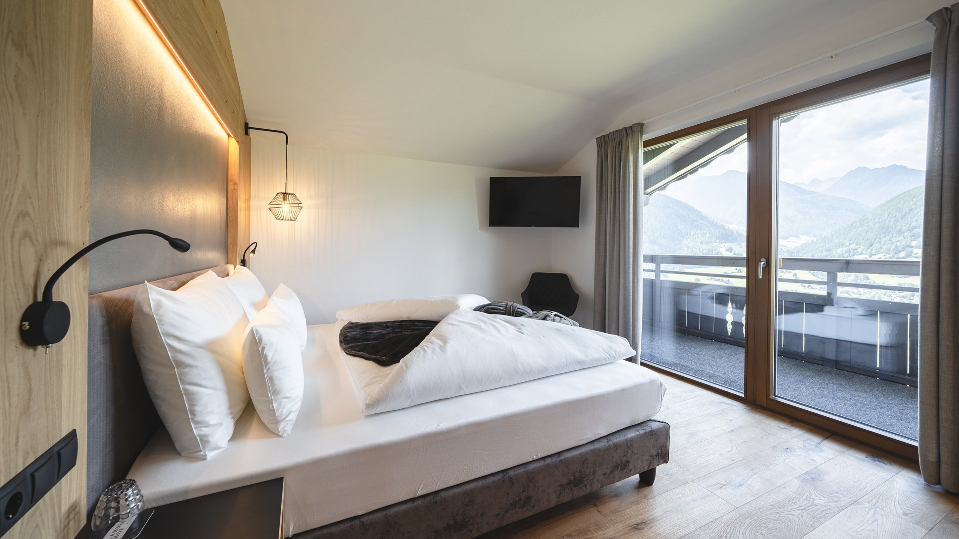 Camera d'albergo moderna con letto grande e vista sulle montagne dalle finestre a tutta altezza