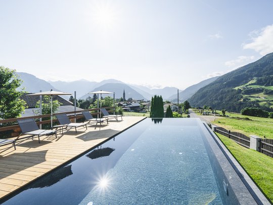 Our hiking and wellness hotel near Sterzing: Lahnerhof Infinity pool with sun loungers and mountain view under a clear sky